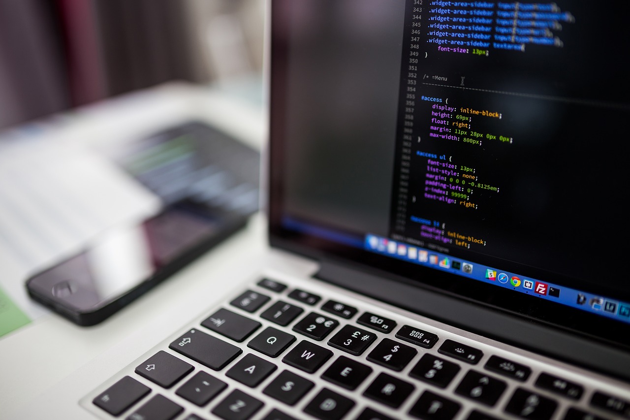 Laptop und Handy auf Schreibtisch mit Computer-Code im Display